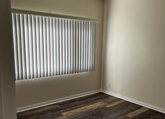 A room with wooden flooring and a window with blinds.