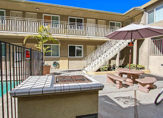 A poolside table with a tiled top is in the foreground of a sunny courtyard.
