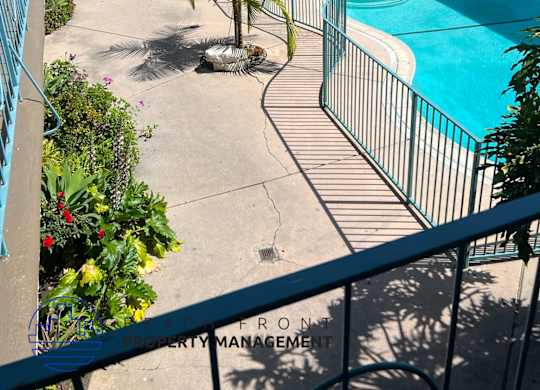 A pool surrounded by a fence and a patio with a table and chairs.