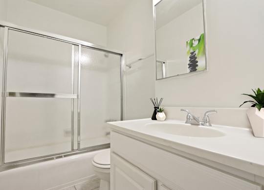 A white bathroom with a glass shower door and a white sink.