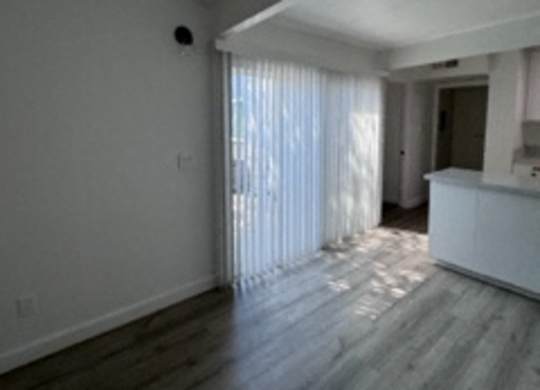 A spacious room with wooden flooring and a window with curtains.