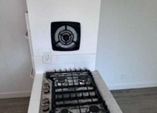 A white stove with a fan on the back is in a room with a white wall.
