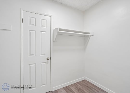 A white door is on the left of a white wall with a shelf on the right.