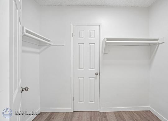 A white door is in the middle of a room with two shelves on the wall.