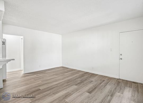 A room with wooden flooring and white walls, with a door on the right side.