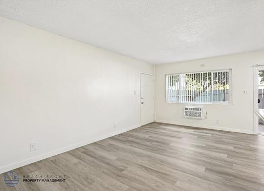 A spacious room with wooden flooring and a window with blinds.