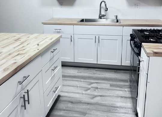 A kitchen with white cabinets and a wooden counter top.