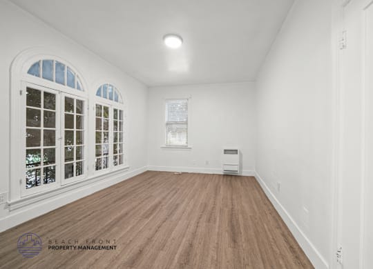 A room with wooden floors and white walls, with a window and a door visible.