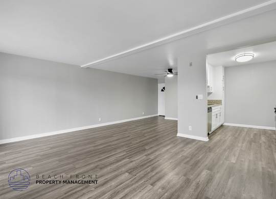 A spacious room with wooden flooring and white walls, with a logo for Beach Front Property Management in the bottom left corner.
