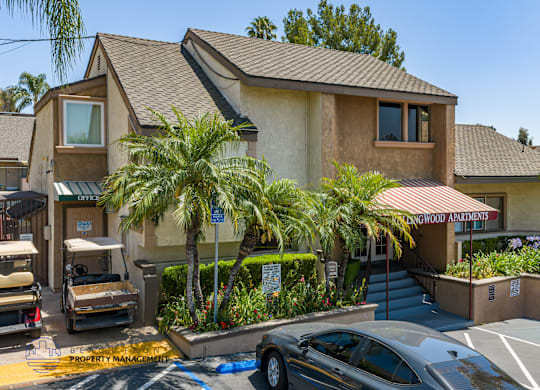 A car is parked in front of a building with a sign that reads "Palmwood Apartments.".