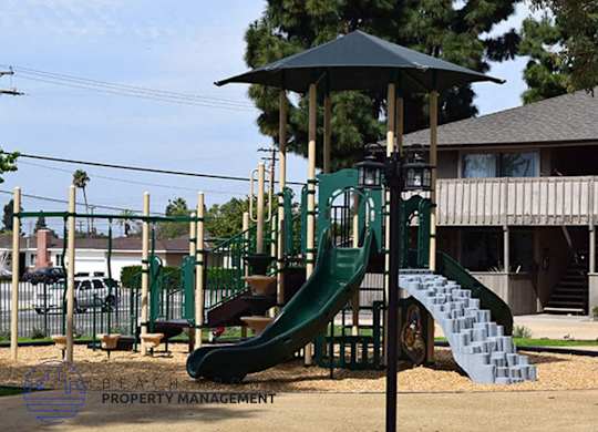 A playground with a green slide and a black umbrella.