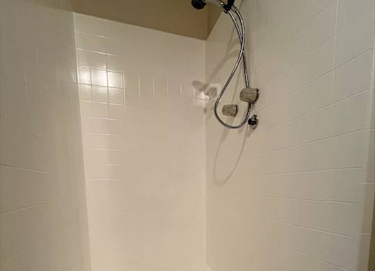A white tiled shower with a drain in the bottom.