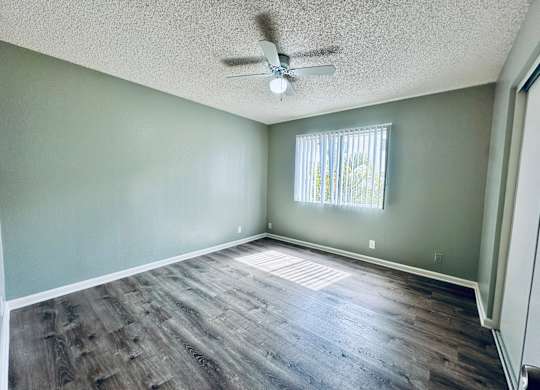 A room with a ceiling fan and a window with blinds.