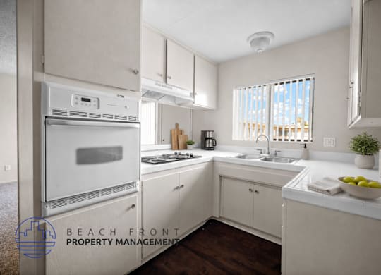 A kitchen with white cabinets and appliances, a window with blinds, and a bowl of fruit on the counter.