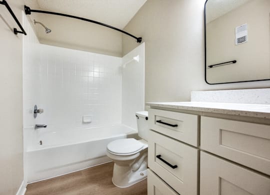 A white toilet sits in a bathroom with a white tub and a white sink.