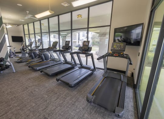 a gym with cardio machines and a tv
