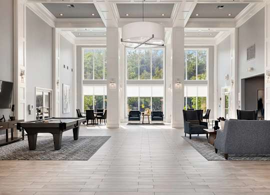 A large, open-concept living room with a pool table and a view of the trees outside the windows.