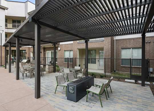 A patio with a black pergola and a table with chairs under it.
