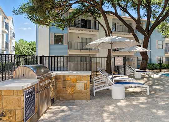 A poolside area with a grill, lounge chairs, and umbrellas.