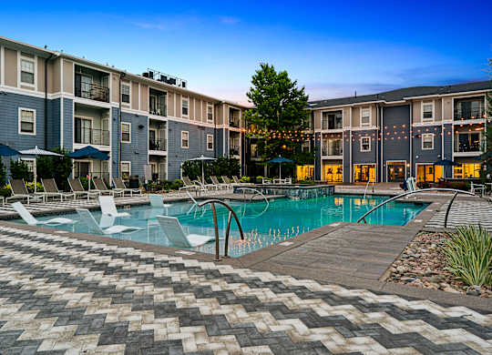 A large swimming pool surrounded by a brick patio and lounge chairs.