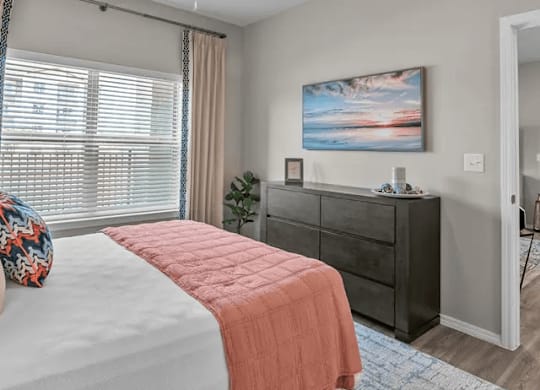A bedroom with a bed, dresser, and a painting on the wall.