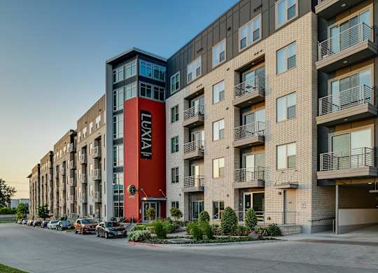 A street view of a row of apartment buildings with cars parked on the side.