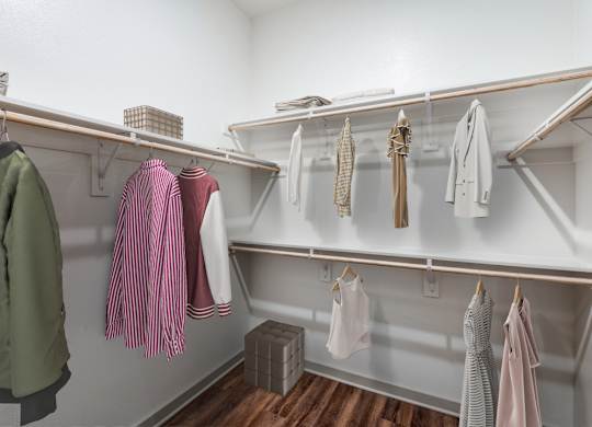 A white closet with clothes hanging on shelves and hangers.