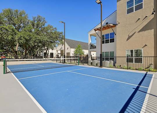 A tennis court is surrounded by a fence and a building.