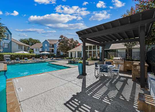 A pool area with a shaded seating area and a building in the background.