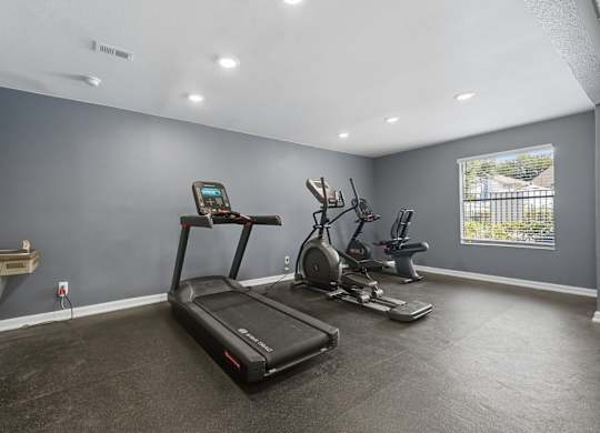 A spacious room with a treadmill, elliptical machines, and a table.