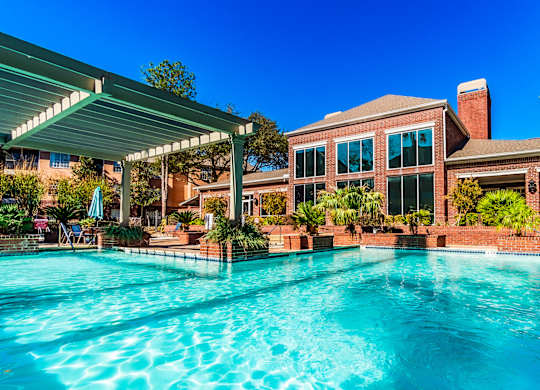 A large swimming pool in front of a house with a covered patio area.