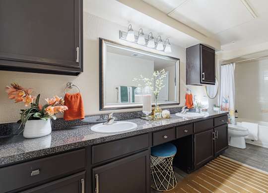 A bathroom with a vanity, sink, mirror, and a chair.