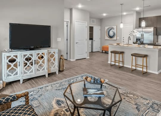 A modern living room with a television, bar area, and a kitchen in the background.
