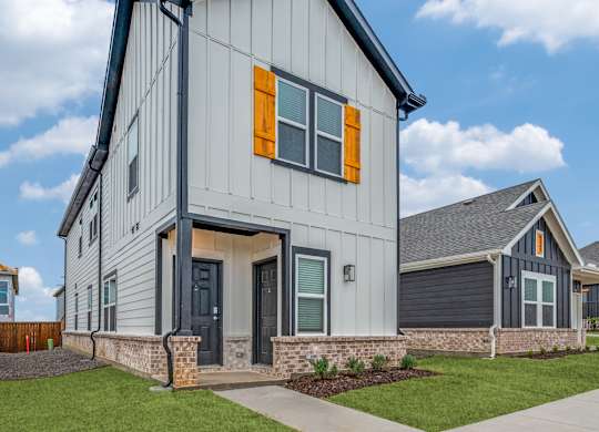 A modern house with a grey and white exterior and orange window shutters.