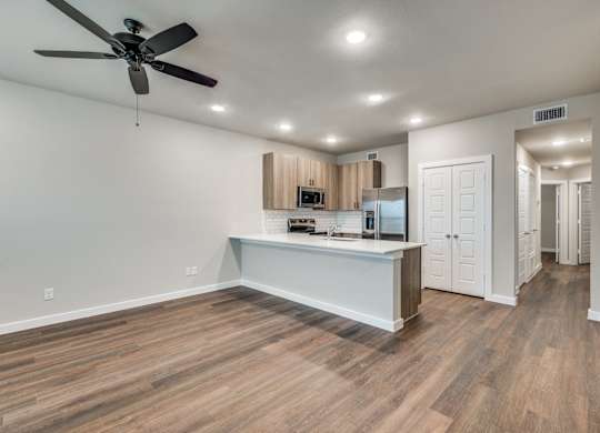 A spacious kitchen with a ceiling fan and wooden flooring.