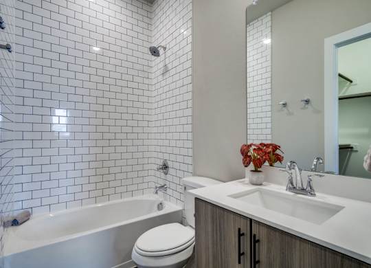 A white toilet sits next to a bathtub in a bathroom with white tiles.
