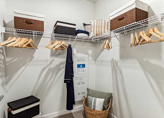 A white closet with clothes hanging and a basket on the floor.