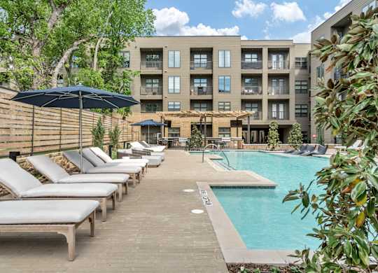 A pool area with sun loungers and a building in the background.