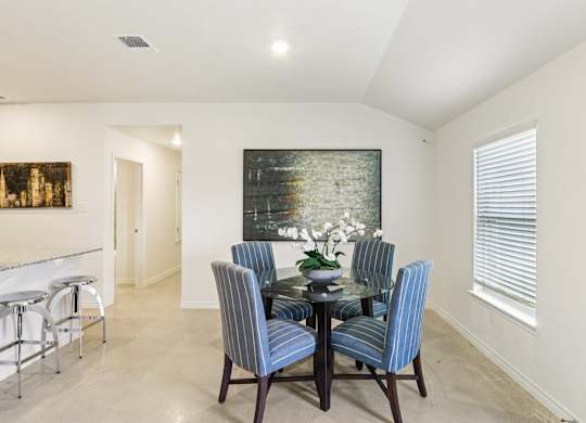 A dining room with a glass table and blue striped chairs.