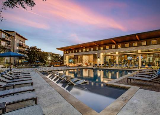 A large outdoor swimming pool with lounge chairs and a building in the background.