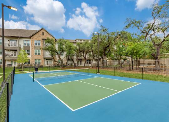 A tennis court is surrounded by a fence and trees.