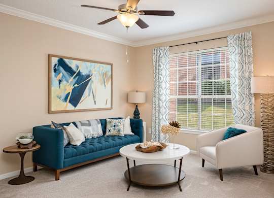 A living room with a blue couch, a white chair, and a painting on the wall.