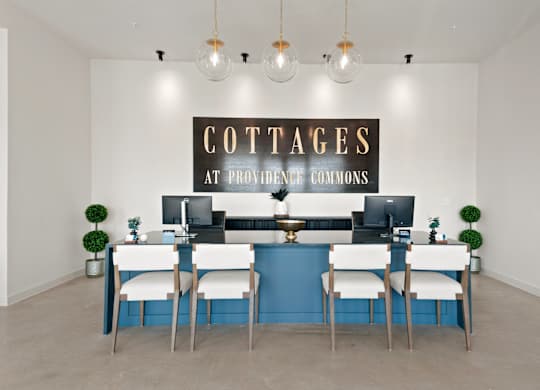 A sign that says "Cottages at Providence Commons" is on the wall above a desk with two computers.