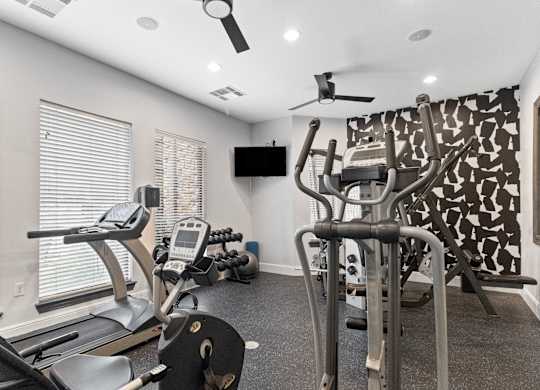 a gym with cardio machines and a tv