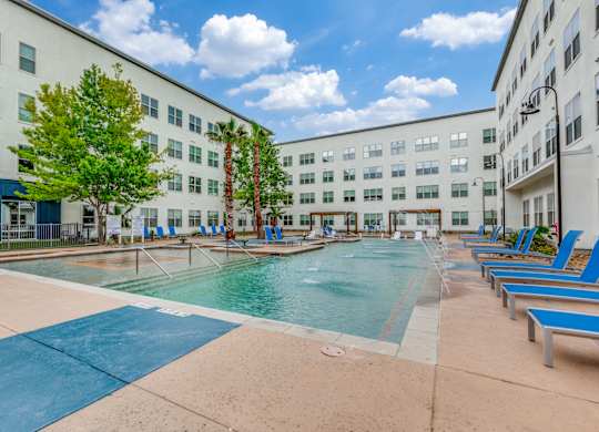 A large swimming pool surrounded by blue lounge chairs and palm trees.