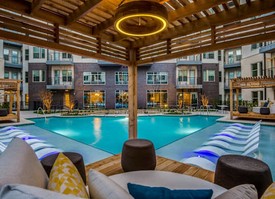 A large outdoor pool area with a wooden pergola and lounge chairs.