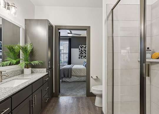 A bathroom with a walk-in shower and a bedroom in the background.