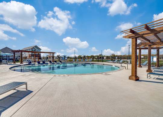 A large outdoor swimming pool surrounded by a wooden pergola and benches.