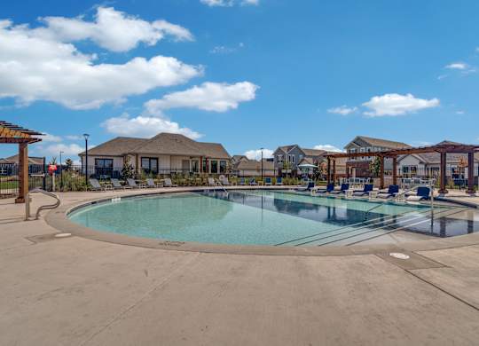 A large outdoor swimming pool surrounded by a fence and a pergola.