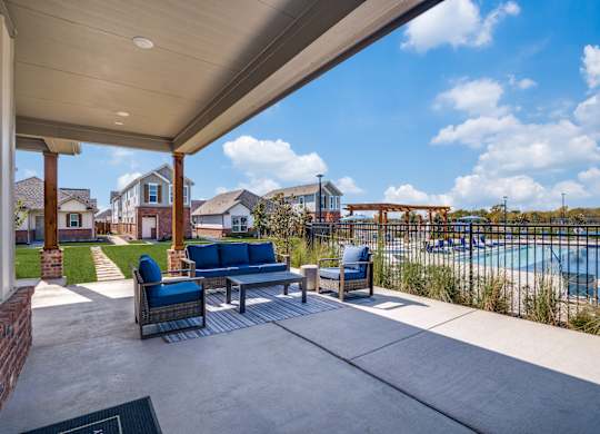 A patio with a couch and chairs overlooking a pool.